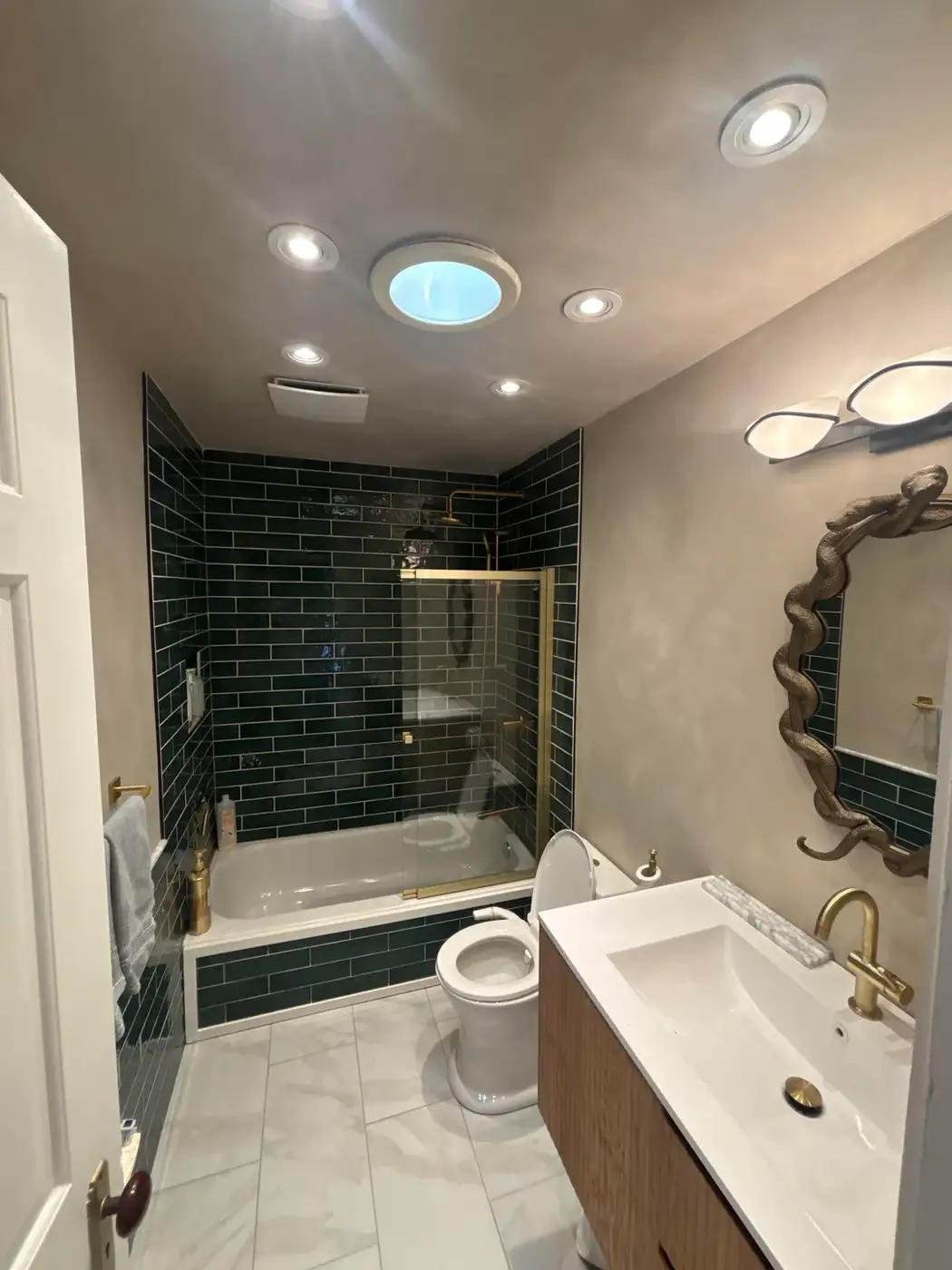Finished bathroom with dark shower tile, white vanity, recessed lighting, mirror, toilet, and tub area