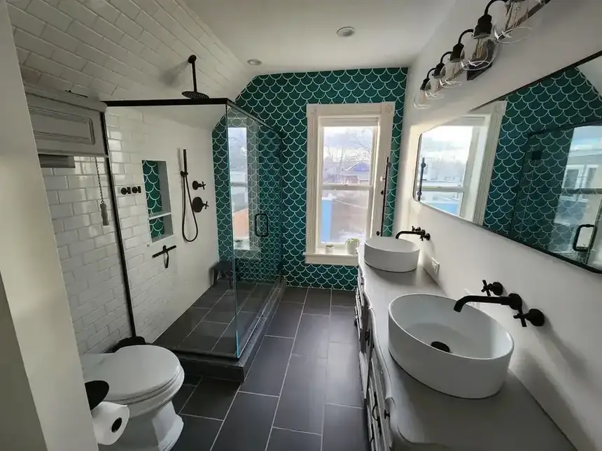 Finished bathroom with double vanity, black fixtures, patterned tile wall, and glass shower