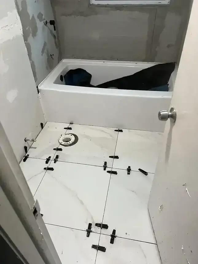 Bathroom floor tile installation progress with white tile layout and visible spacers