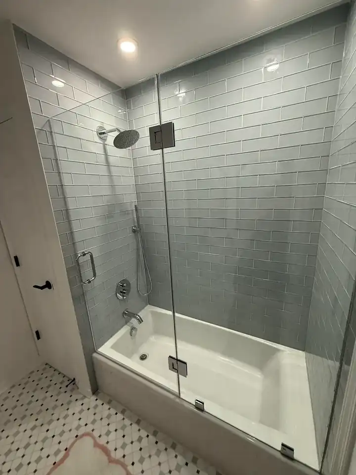 Finished bathroom with gray tile tub surround, glass enclosure, recessed lighting, and patterned floor