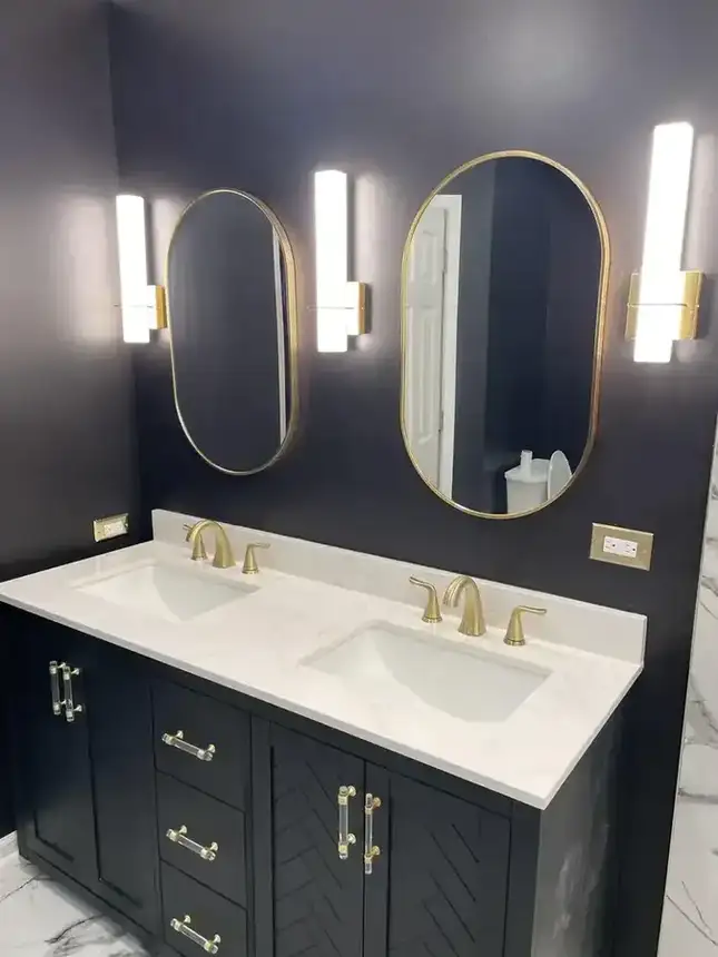 Bathroom vanity with navy wall, double mirrors, white counter, brass fixtures, and lighting