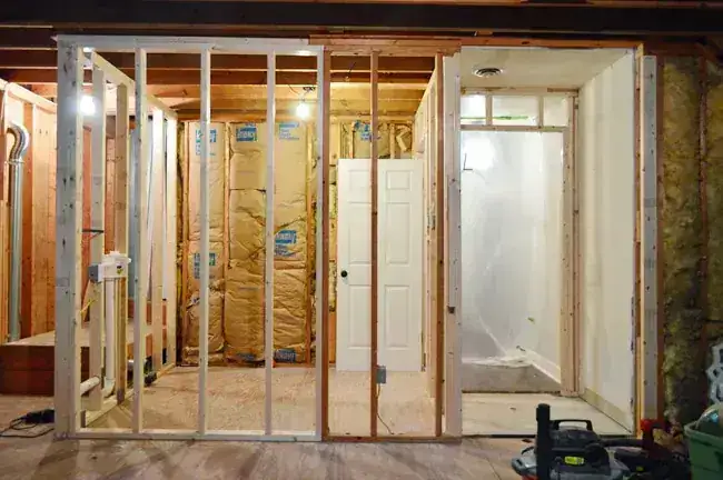 Interior framing progress with studs, door opening, and exposed wall cavity