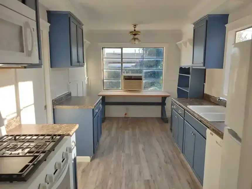 Finished kitchen with blue cabinets, wood floor, window, counters, and appliances