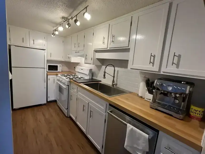 Finished white galley kitchen with refreshed cabinets, counters, flooring, and appliances